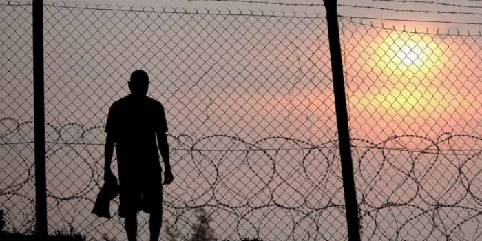 Man in silhouette at sunset behind razor wire holding shirt in his right had. Shadow prisoners at VCBR are subject to an improper imbalance of power in so-called "sex offender treatment."