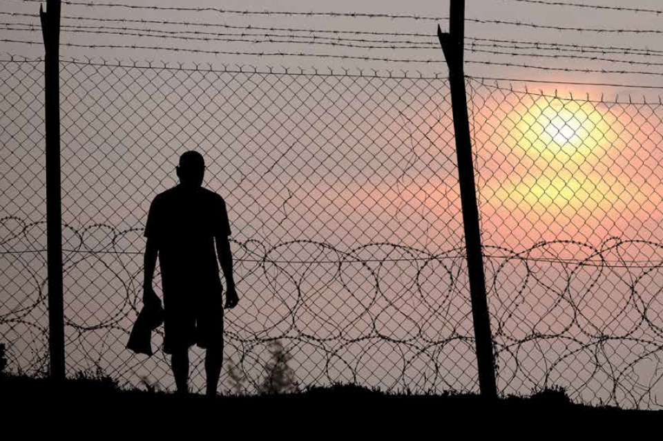 Man in silhouette at sunset behind razor wire holding shirt in his right had.  Shadow prisoners at VCBR are subject to an improper imbalance of power in so-called "sex offender treatment."